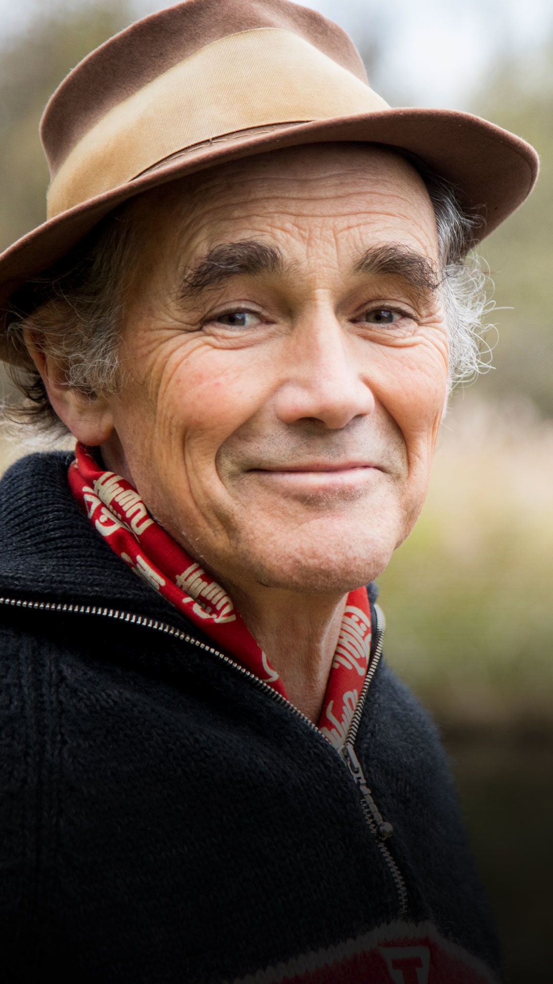 New WWT ambassador Sir Mark Rylance smiling at the camera, with a wetland backdrop