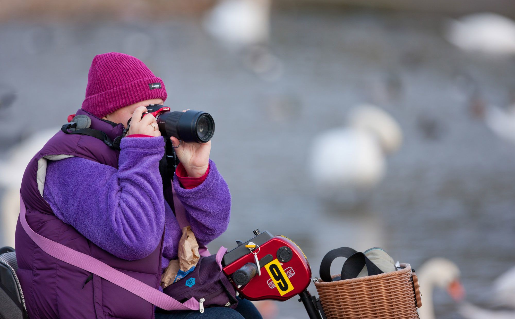 A woman taking a photograph from her mobility scooter with blurred water and swans in background